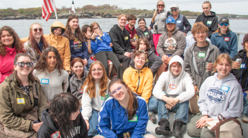 Students sit on a boat and pose for the camera.